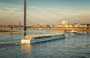 A serene cityscape with cruise ships on a river under a modern bridge at sunset.